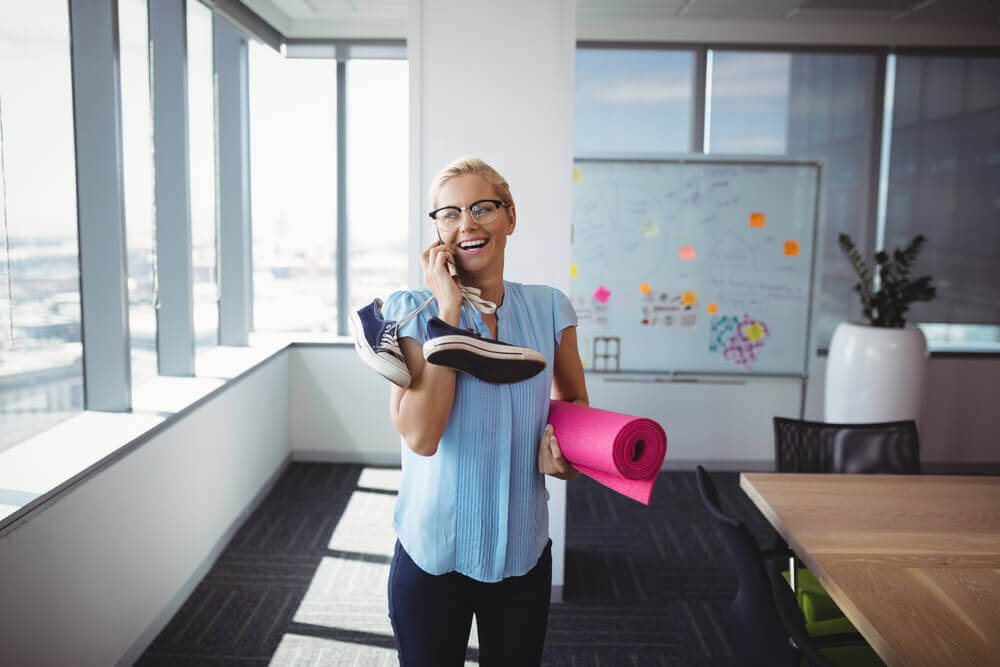 Woman on phone in office holding gym gear