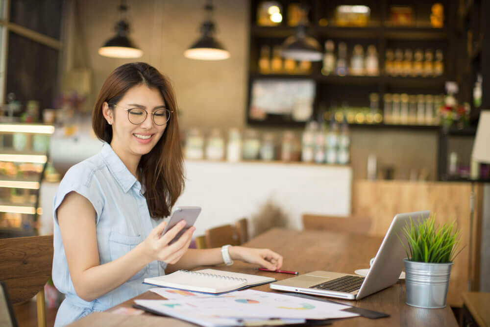 Woman in cafe working with laptop and looking at phone