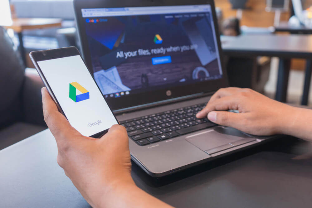 Hand holding phone with Google Drive app and Google Drive open on laptop