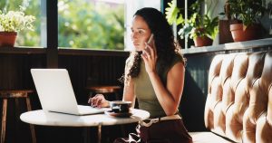 Woman on phone with laptop at cafe