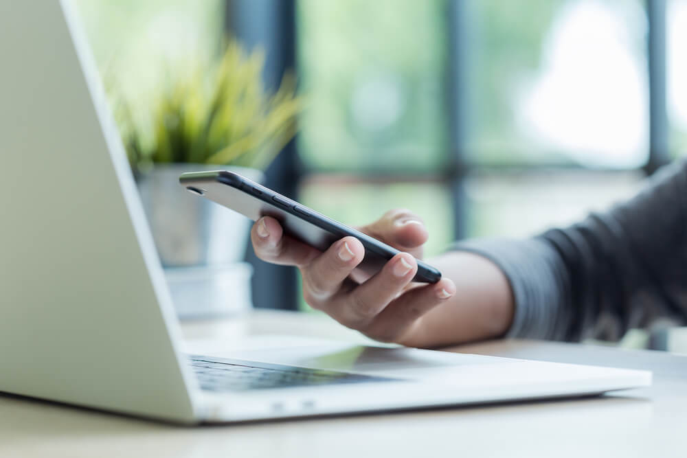 Hand holding phone near laptop