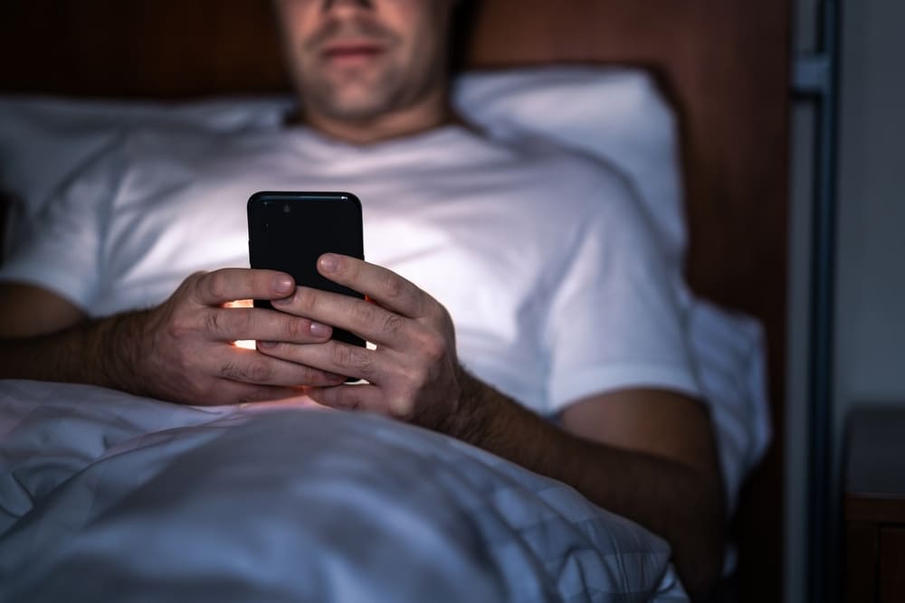 Man looking at phone and sending work emails at night in bed