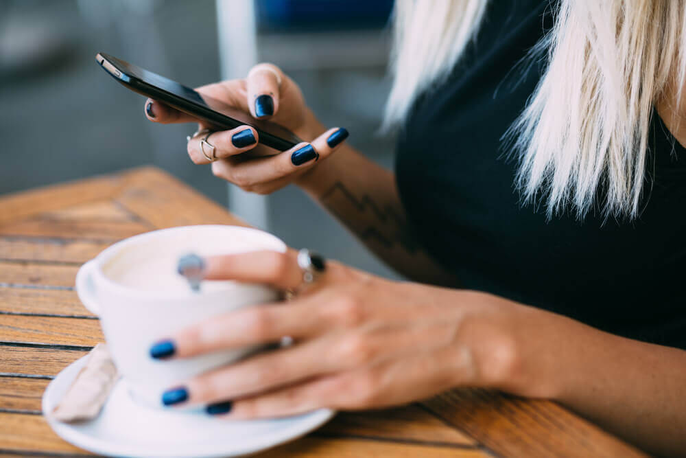 Woman using phone with coffee in other hand