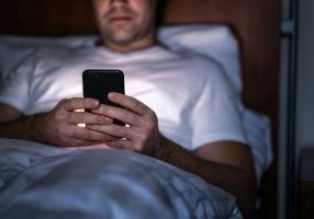 Man looking at phone and sending work emails at night in bed